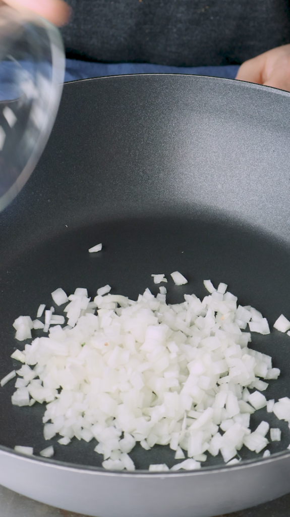 Next add diced onion, tomato sauce, tomato paste, minced garlic, turmeric, and coriander to a large pan. 